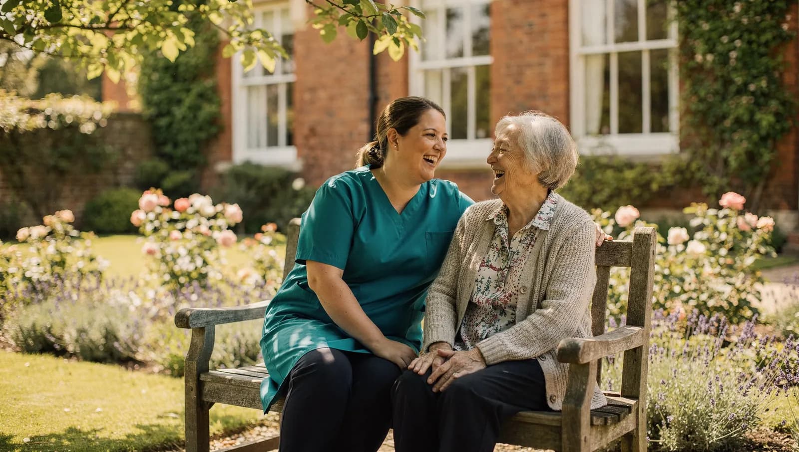 A care worker and a resident laughing together on a garden bench